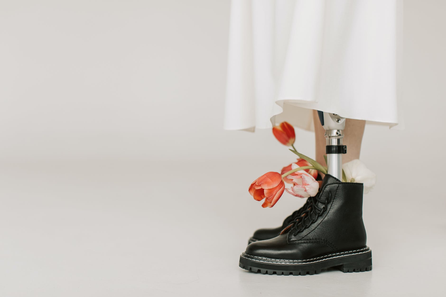 Photo of a pair of boots being worn by someone with one flesh foot and one prosthetic foot. There are tulips in the boot with the prosthetic foot to show the beauty of diversity.